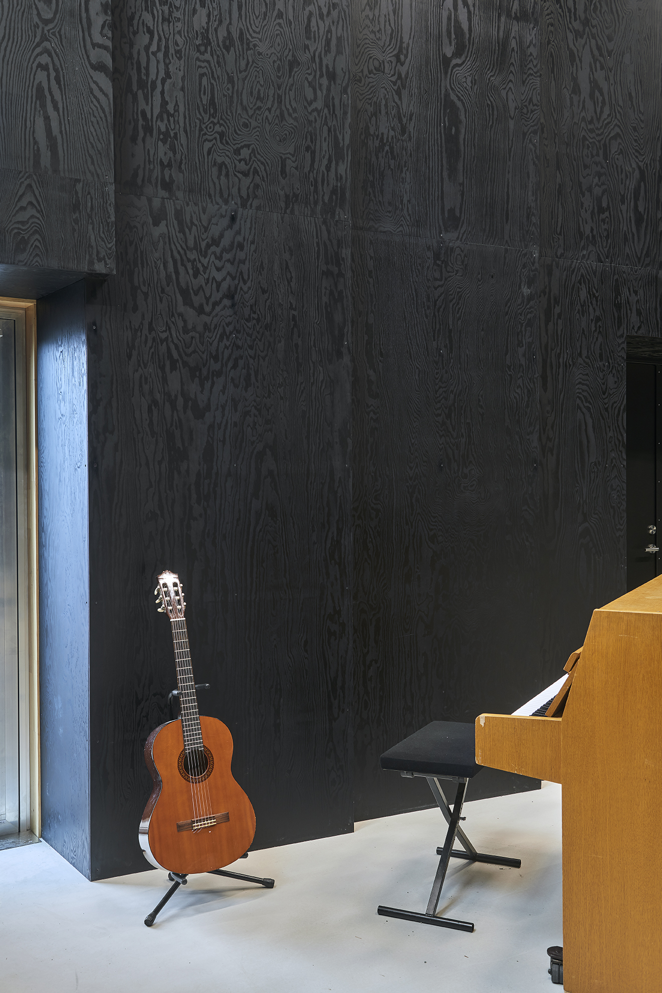 Musikrum med klaver og guitar, mes sorte træpaneler på væg