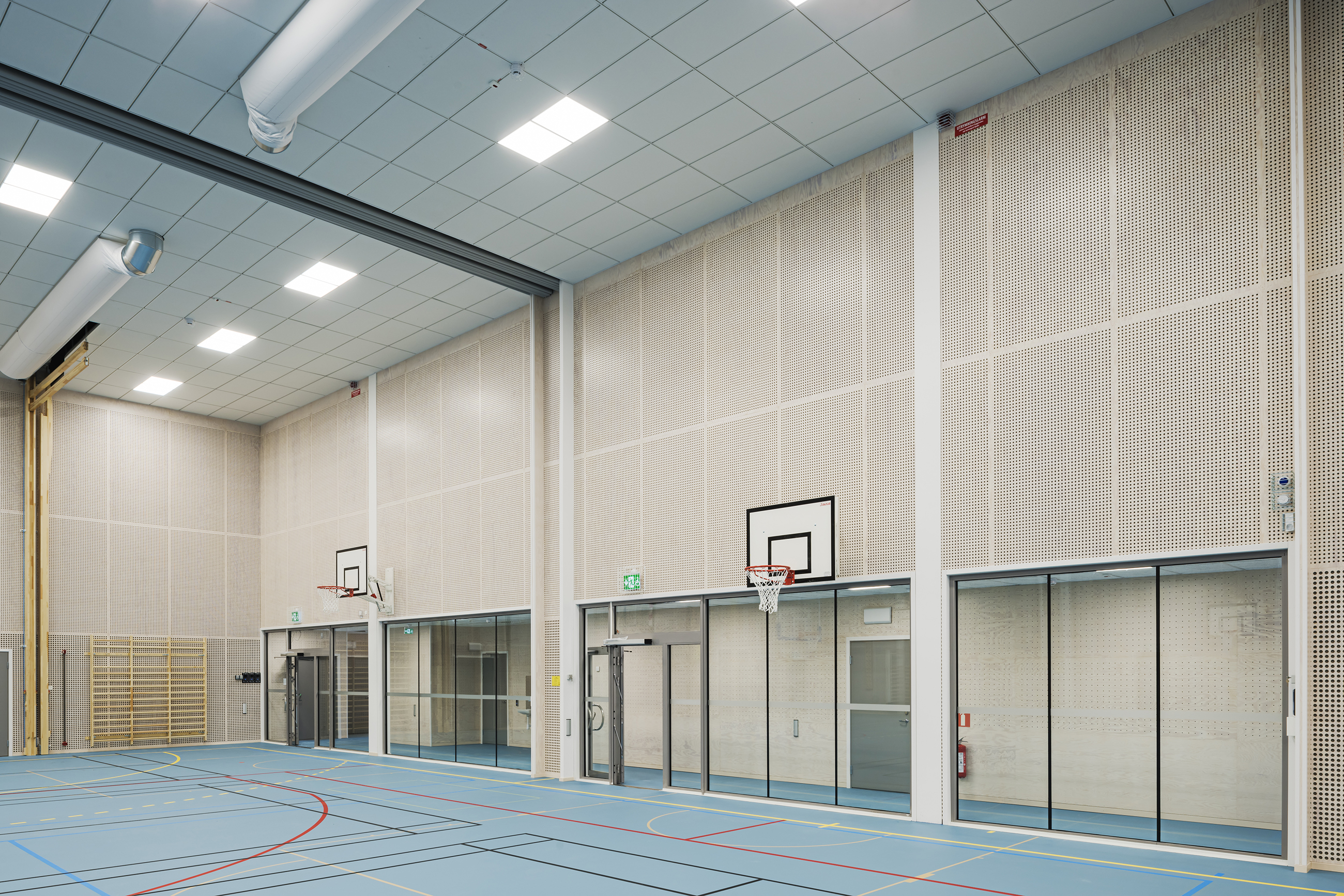 Gymnastiksal med perforerede paneler på væggene og blåt gulv