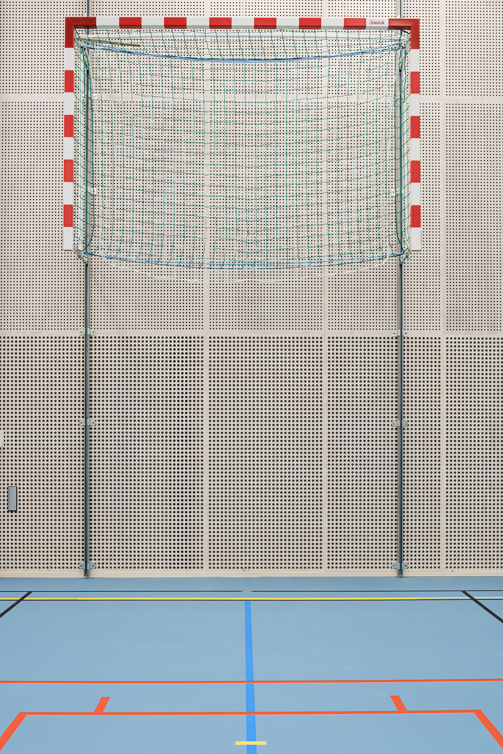 Gymnastiksal med perforerede paneler på væggene, blåt gulv og hævebart håndboldmål