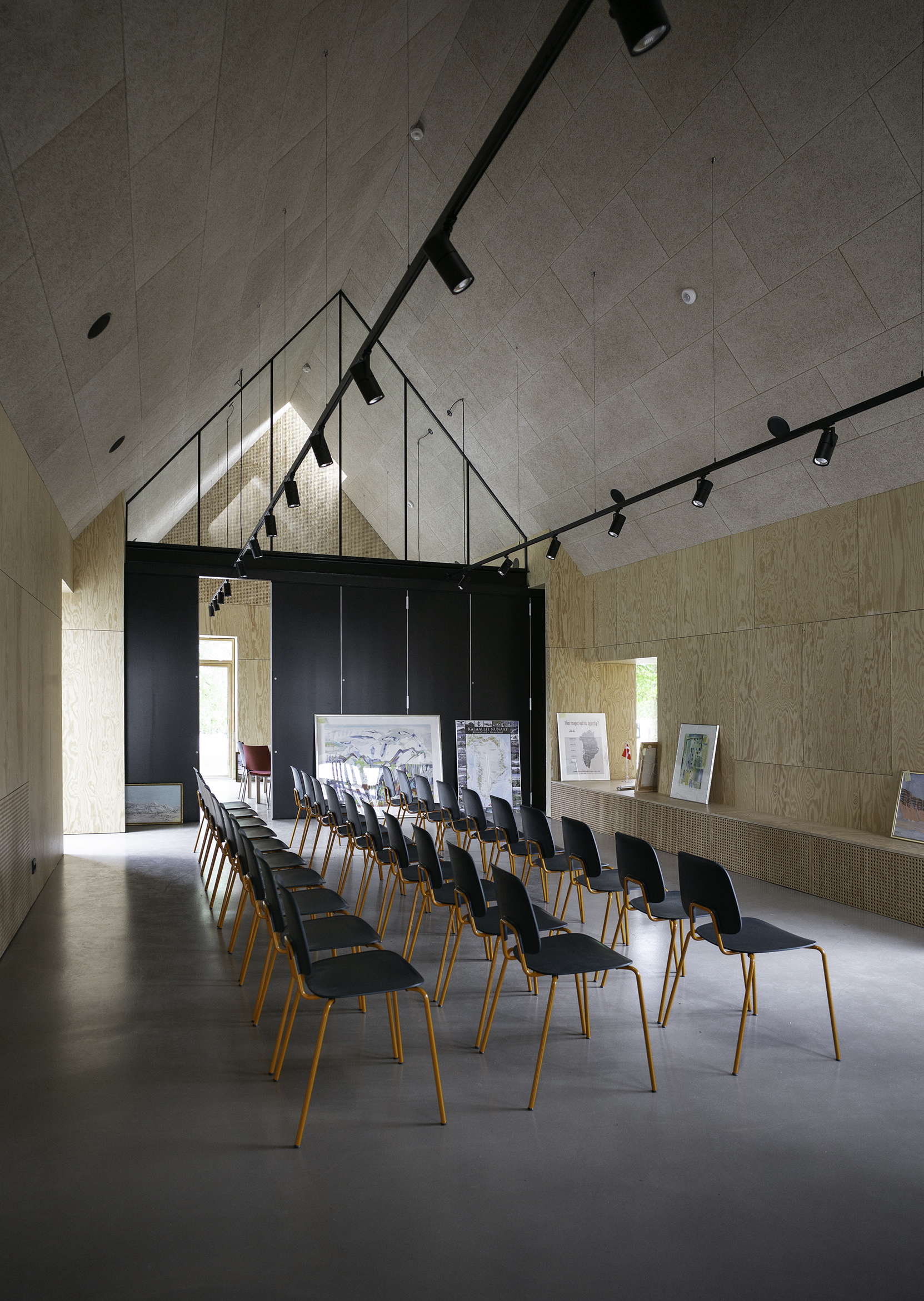 Samlingsrum med loft til kip med glatte træpaneler på vægge og stole foran lille scene
